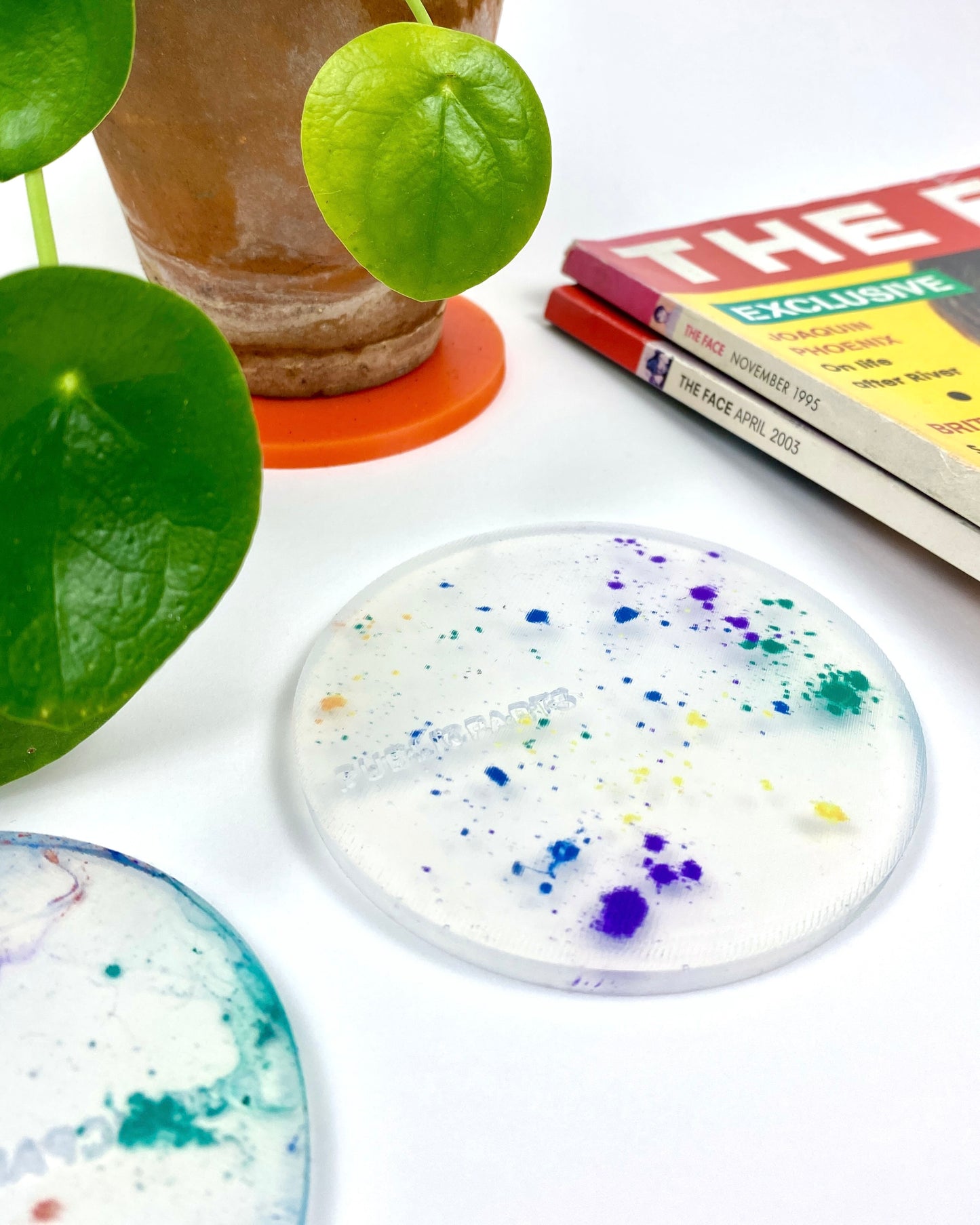 Speckled silicone coaster on a white surface with a plant and magazines in the background
