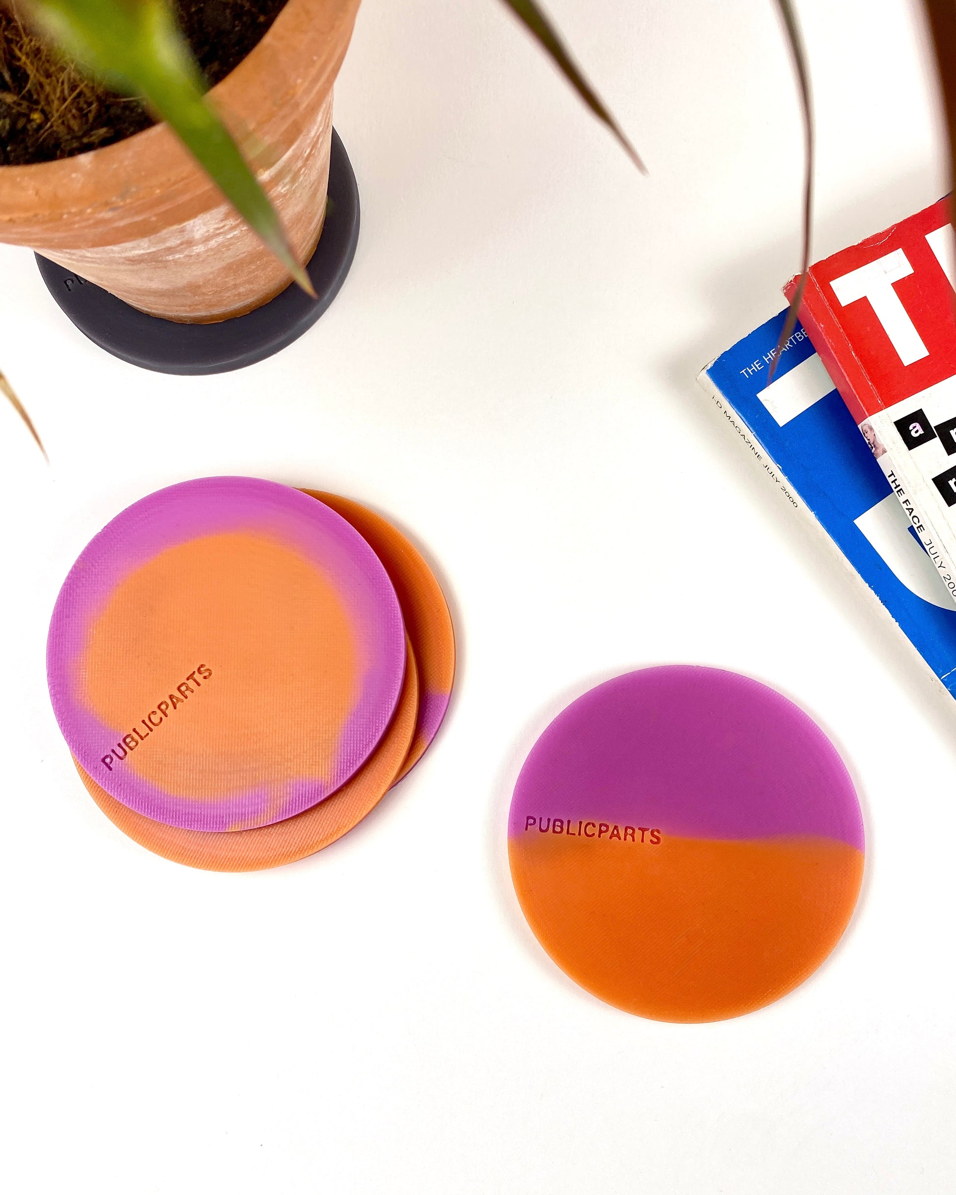 Heat-reactive silicone coasters in orange and pink styled with plant and magazines.