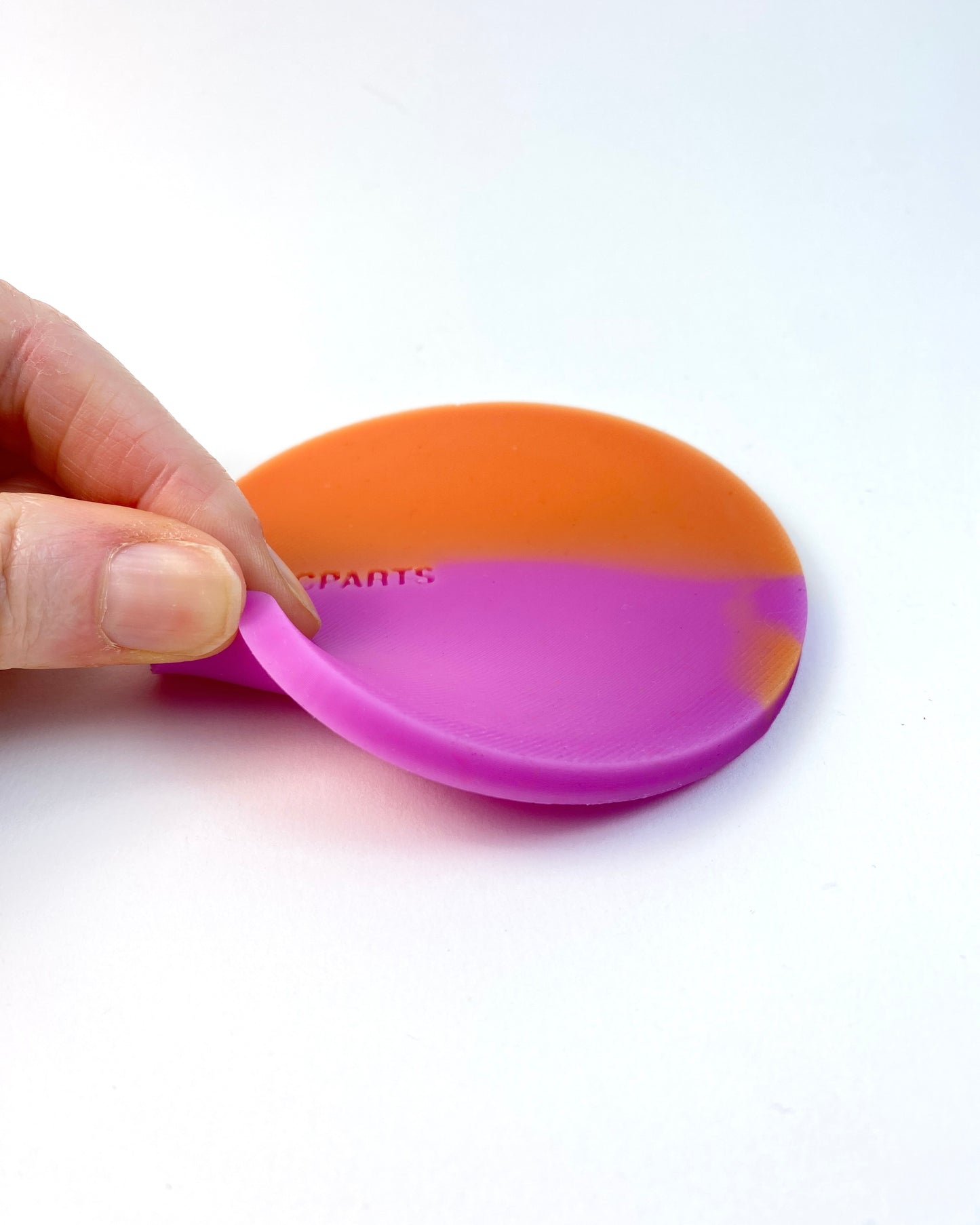 Flexible silicone coaster bent by hand, showing soft thermochromic material.