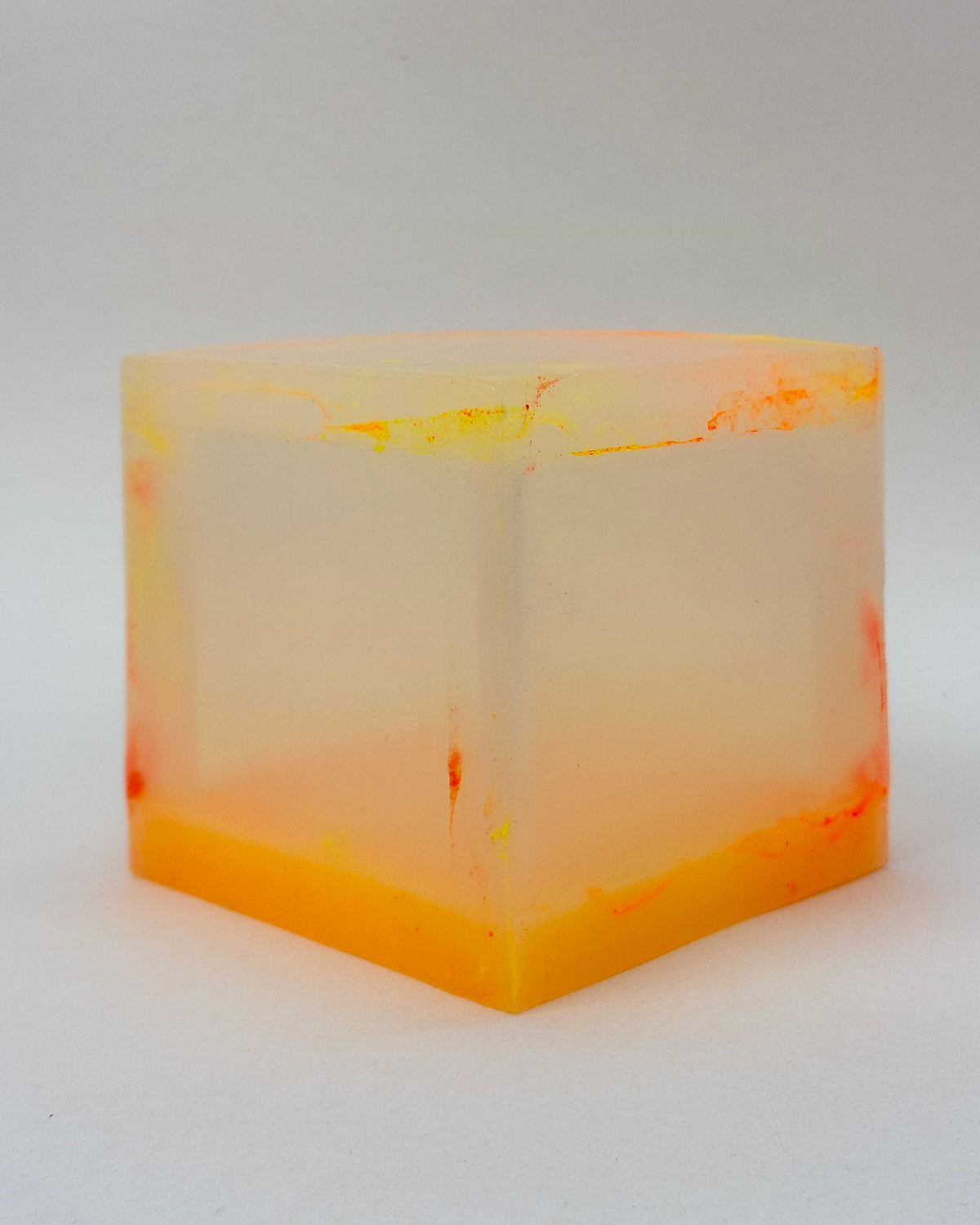 A translucent square silicone lamp with a frosted off-white center and vibrant orange and yellow marbled patterns along the top and bottom, photographed on a neutral light gray background.