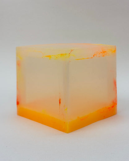 A translucent square silicone lamp with a frosted off-white center and vibrant orange and yellow marbled patterns along the top and bottom, photographed on a neutral light gray background.